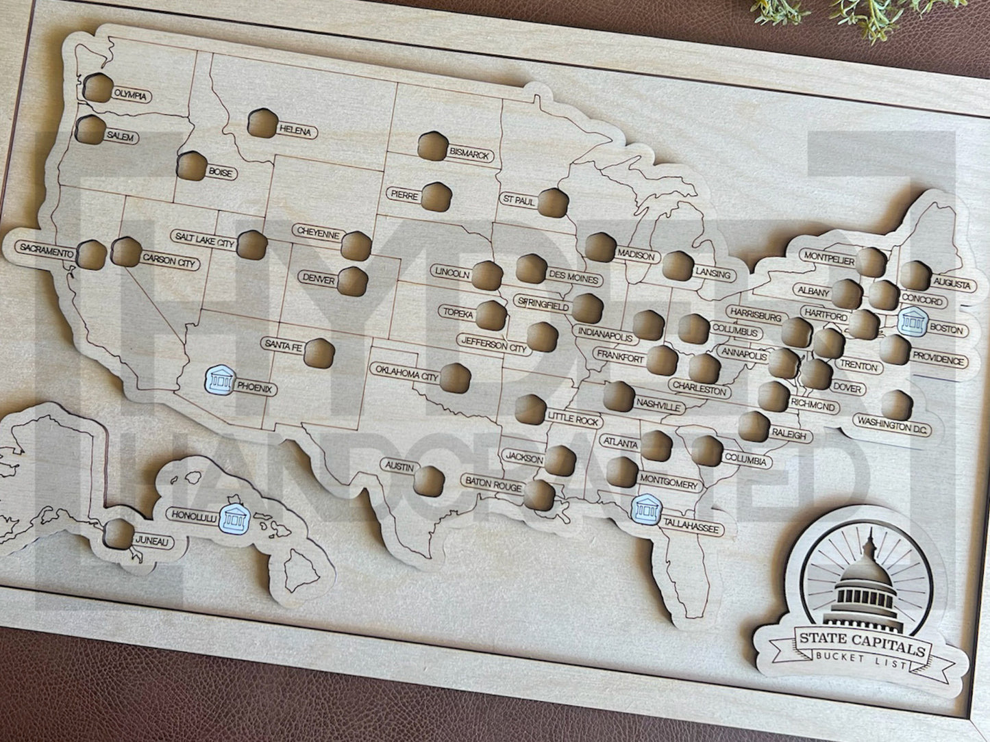 A framed State Capitals bucket list map with a natural wood finish, white tokens, and a sawtooth hanger. The map shows a list of state capitals and has a seal stamp with the text 'STATE CAPITALS' on it.
