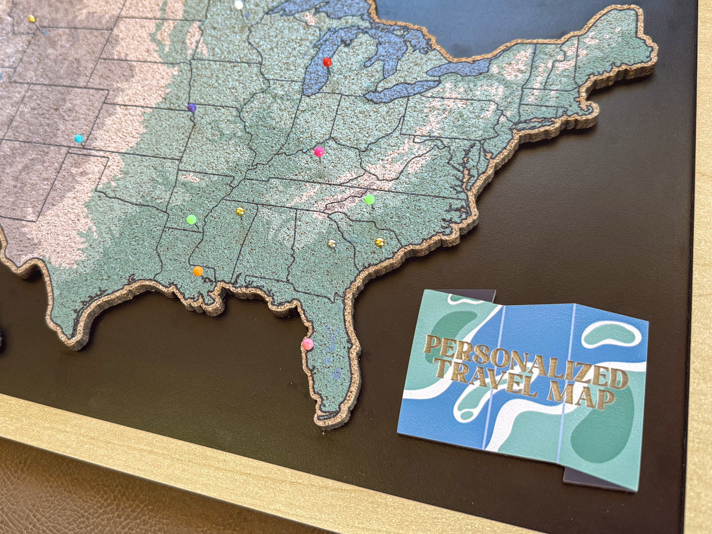 Map of the United States with pins and a personalized travel map card on a wooden surface.