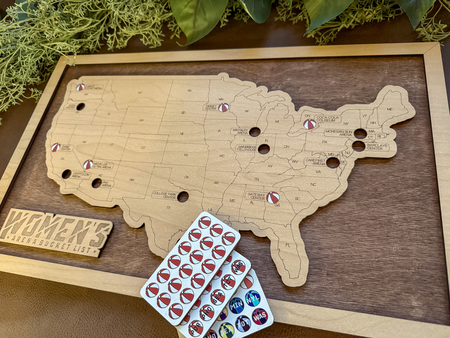 Wooden map of the United States with pins and a plank of sticker tokens on a wooden surface.