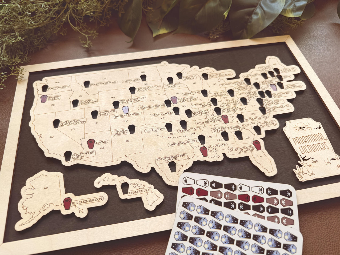 Map of the United States with pins and a set of coffin tokens on a wooden surface.