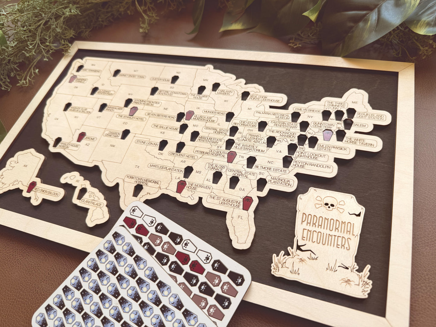 Map of the United States with ghostly figures on a wooden board, accompanied by a box of decorative tracking tokens.