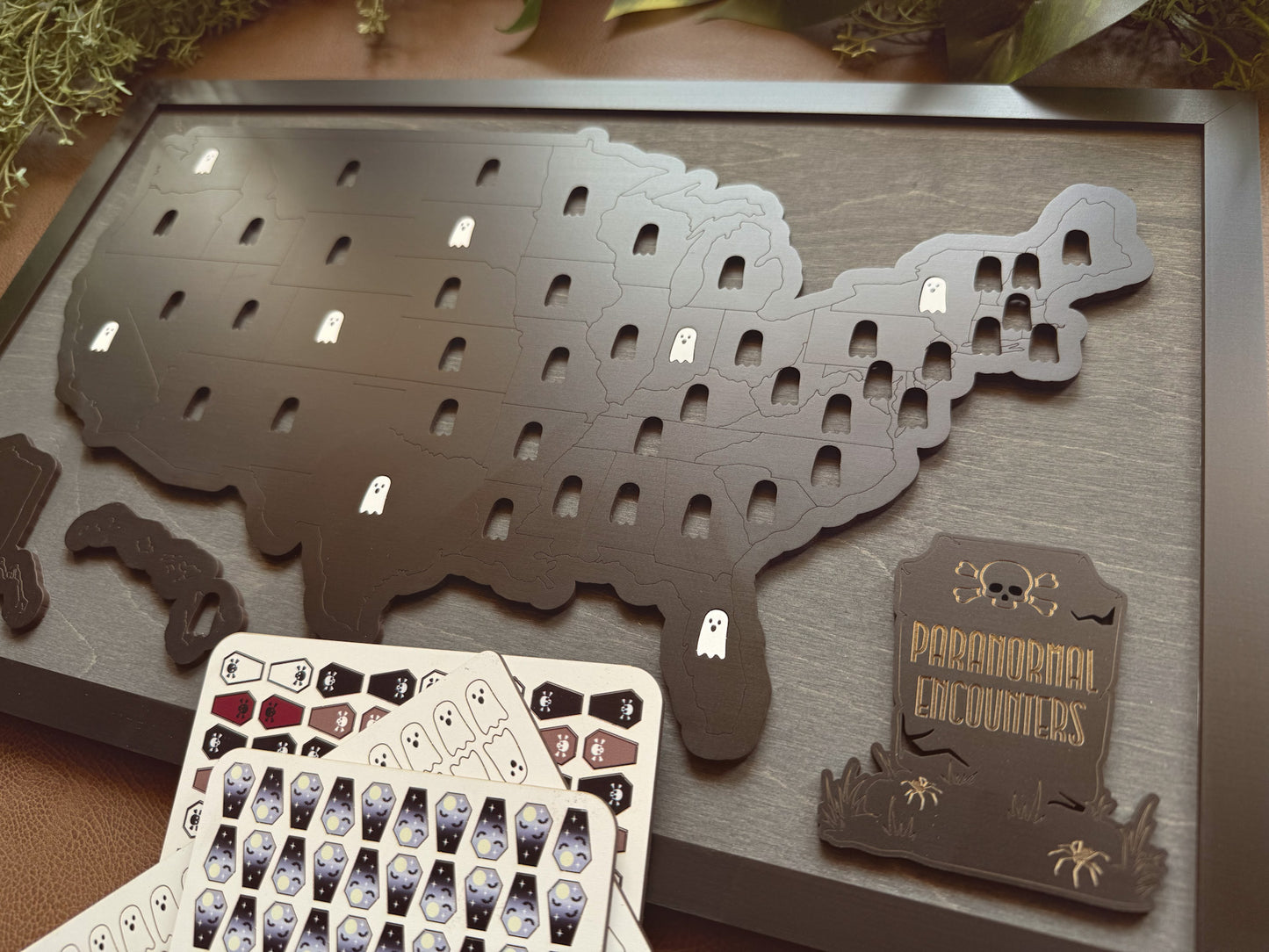 Map of the United States with cut-out states on a wooden surface, accompanied by a card of tokens for tracking