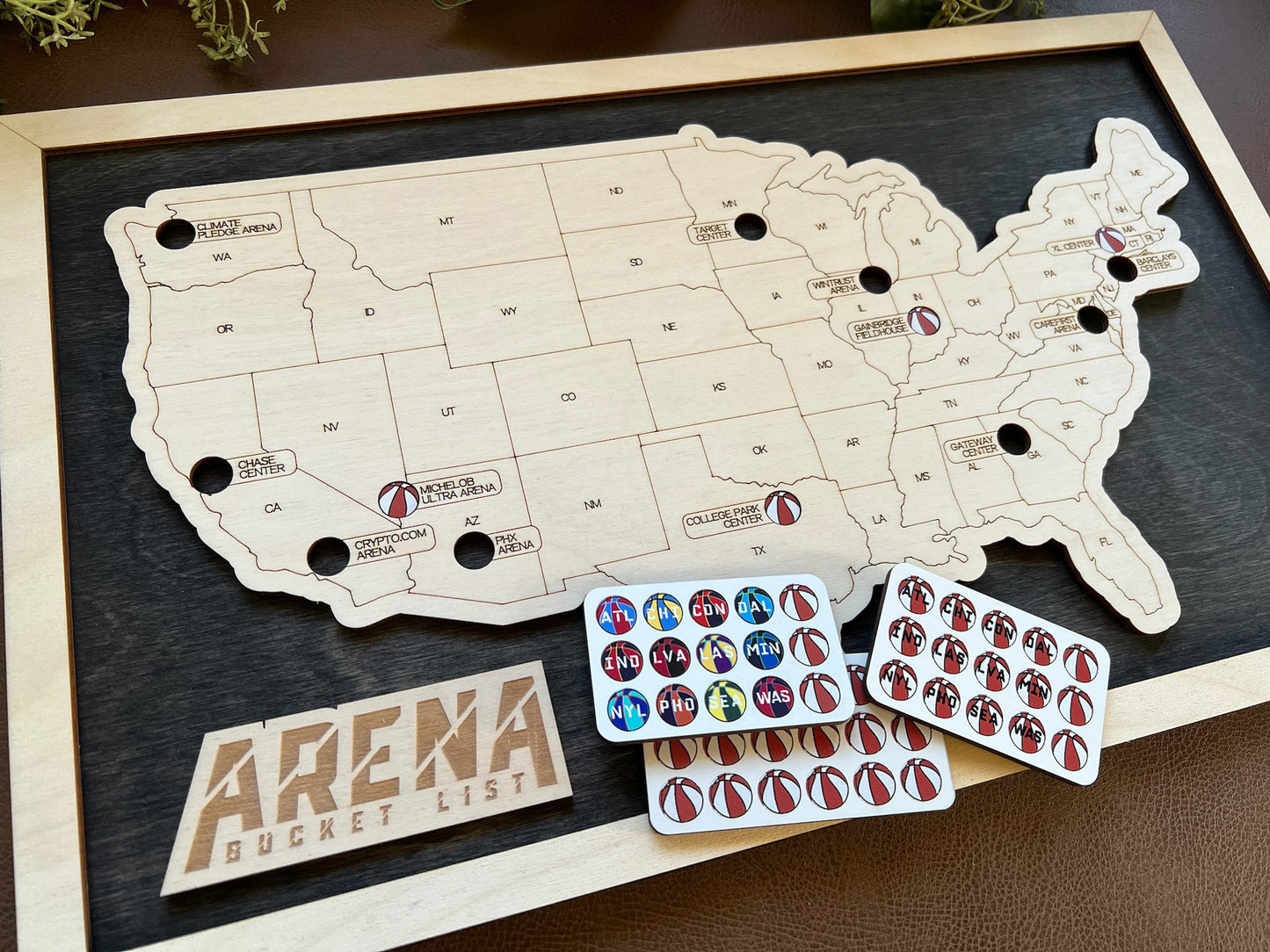Wooden map of the United States with Arena Bucket List stickers on a dark surface