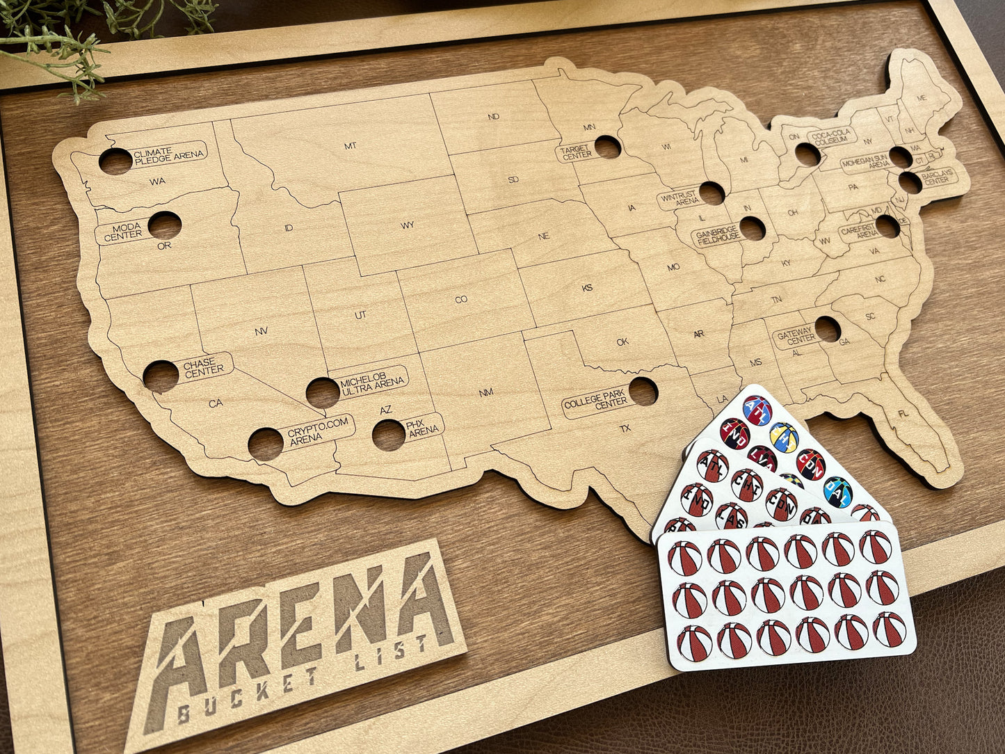 Wooden map of the United States with 'Arena Bucket List' branding and a small card with stickers on a wooden surface.