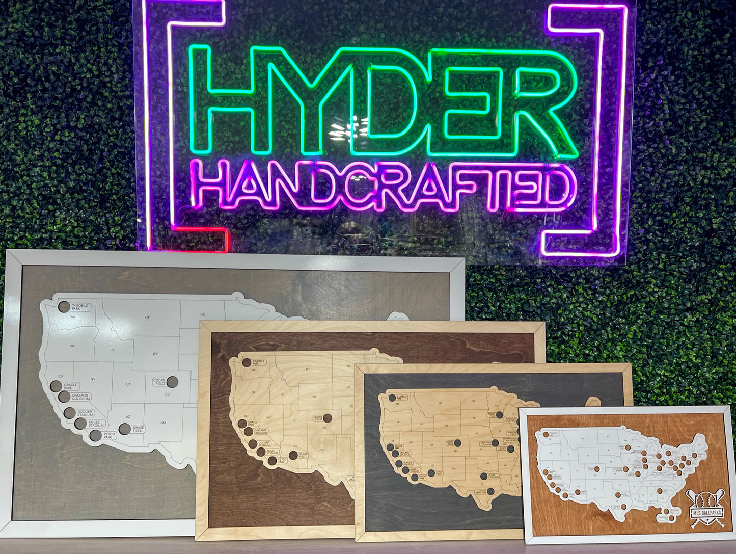 A collection of sport-themed tracking maps with pins, displayed in front of a neon sign that reads 'Hyder Handcrafted'.