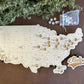 Handcrafted wooden map of the United States in a floating style design, with white baseballs used to mark locations on the map, accompanied by a bag of additional baseball-shaped tokens.