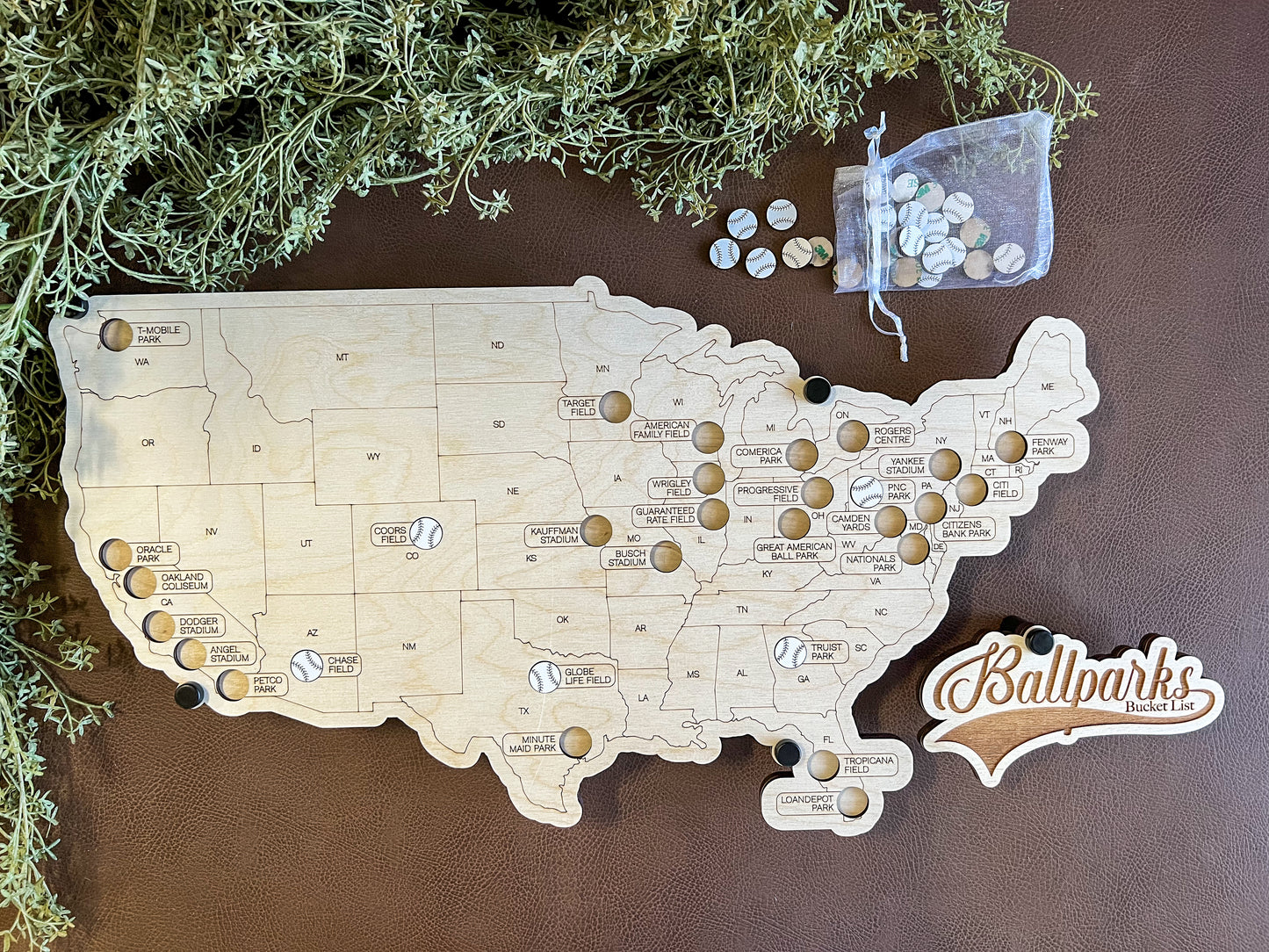 Handcrafted wooden map of the United States in a floating style design, with white baseballs used to mark locations on the map, accompanied by a bag of additional baseball-shaped tokens.