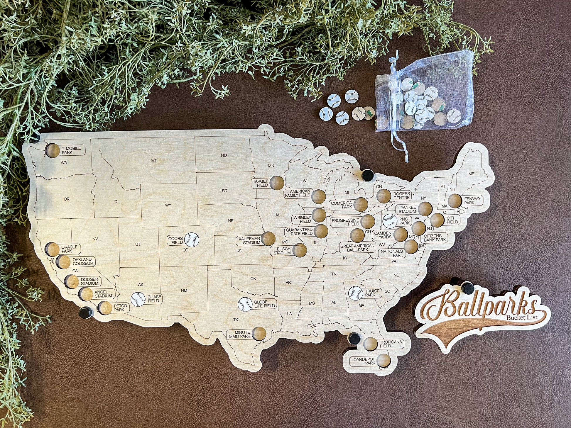 Handcrafted wooden map of the United States in a floating style design, with white baseballs used to mark locations on the map, accompanied by a bag of additional baseball-shaped tokens.