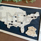 A wall-mounted map showcasing the locations of Presidential Libraries in the United States with a wooden frame and markers. The map is labeled with 'Bucket List' and 'Presidential Libraries'. Black stain background