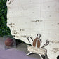 Handcrafted wooden multi-sport map with a football and baseball decoration, displayed on a stand against a greenery backdrop.