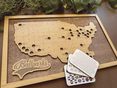 Wooden map of the United States with cut-out states, 'Ballparks Bucket List' branding, and a stack of cards on a wooden surface.