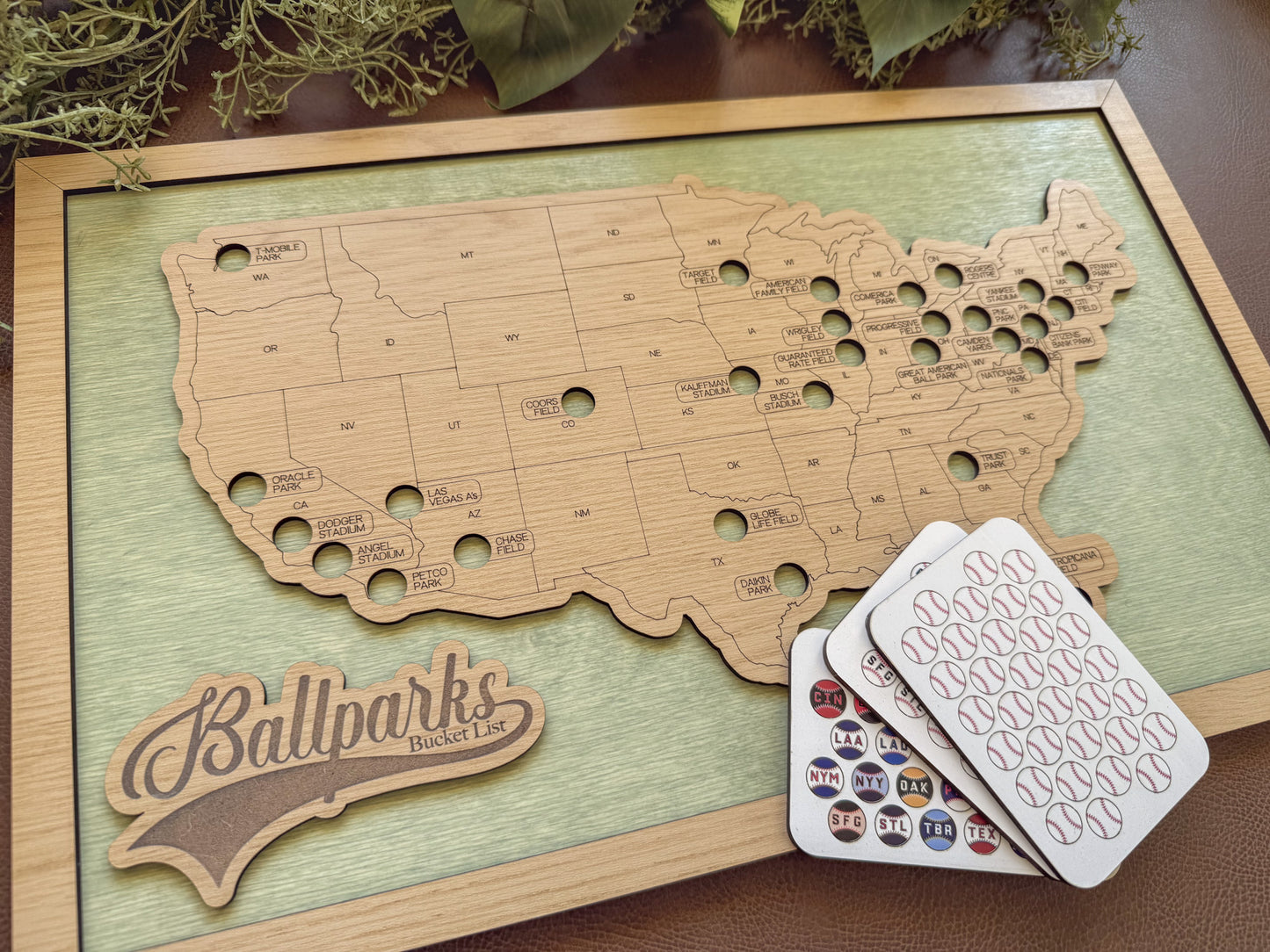 Wooden map of the United States with cut-out states, 'Ballparks Bucket List' branding, and cards on a wooden surface.