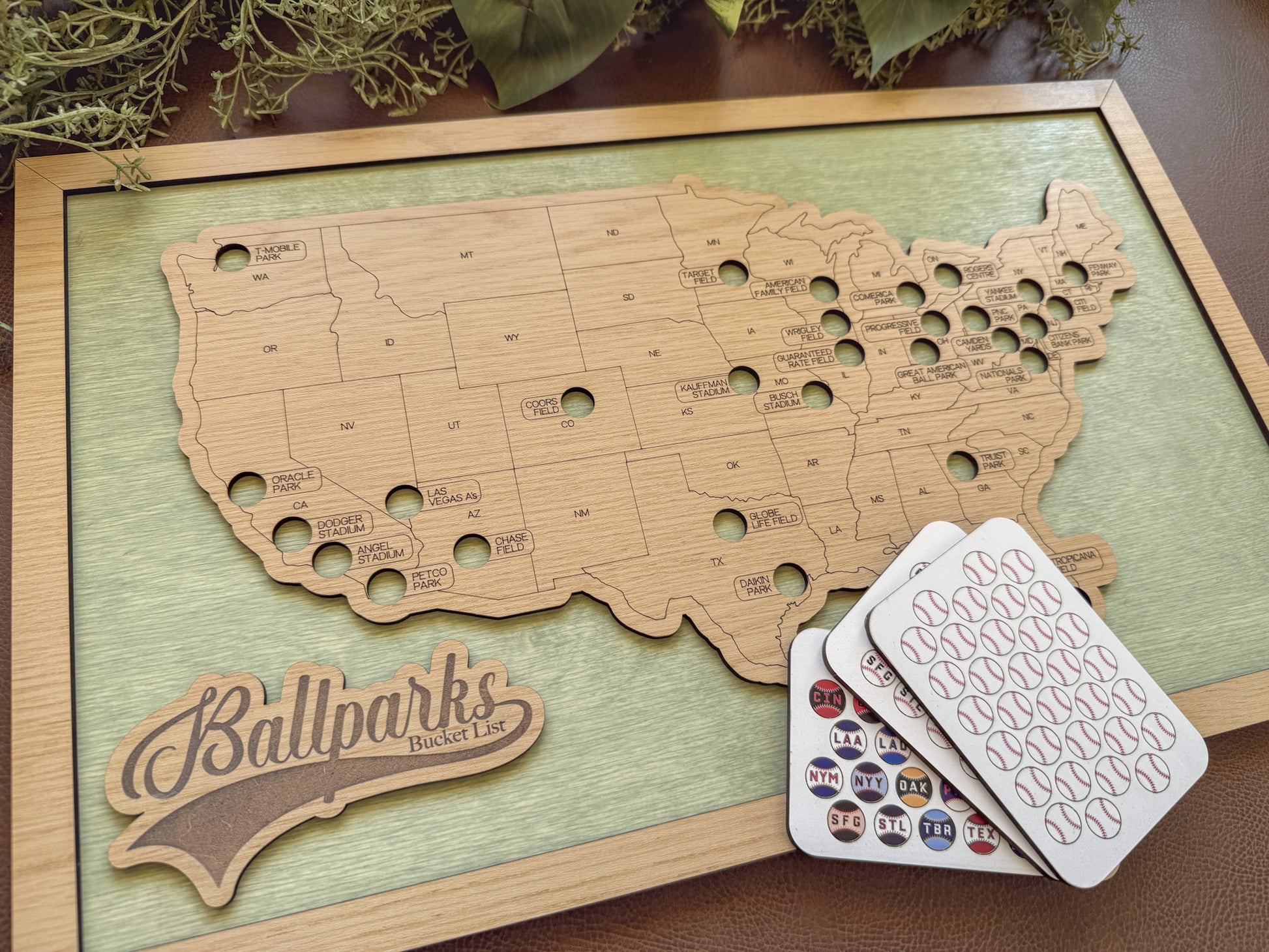 Wooden map of the United States with cut-out states, 'Ballparks Bucket List' branding, and cards on a wooden surface.