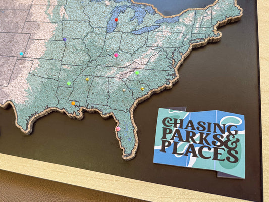 Map of the United States with pins and a card titled 'Chasing Parks & Places' on a dark surface.