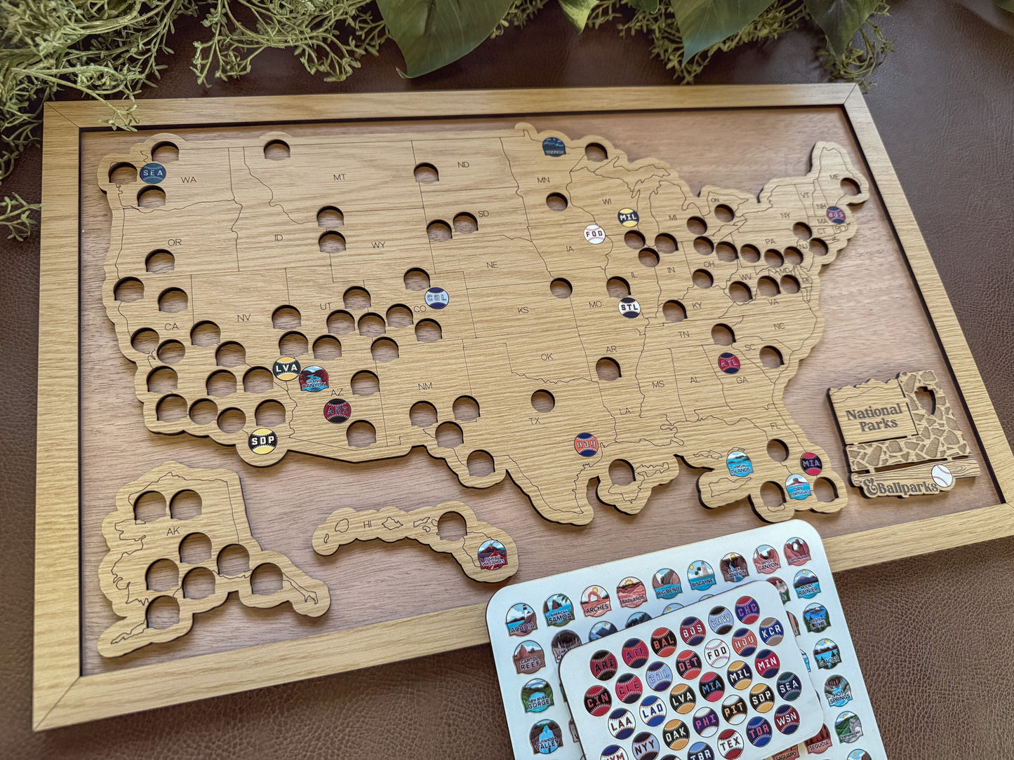 Wooden map of the United States with pins and a card of stickers on a wooden surface.