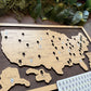 Wooden map of the United States with pins on a wooden surface with greenery.