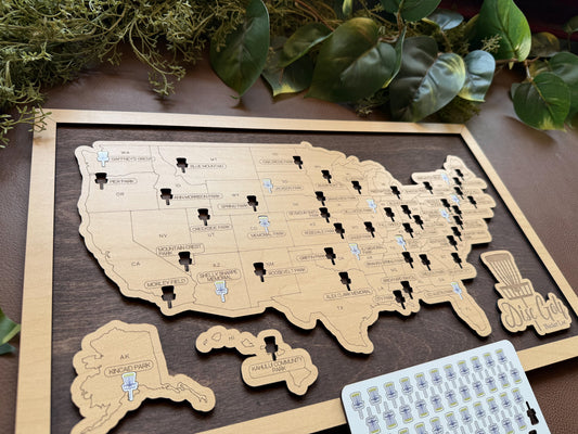 Wooden map of the United States with pins on a wooden surface with greenery.