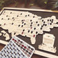 Map of the United States with ghostly figures on a wooden board, accompanied by a box of decorative tracking tokens.