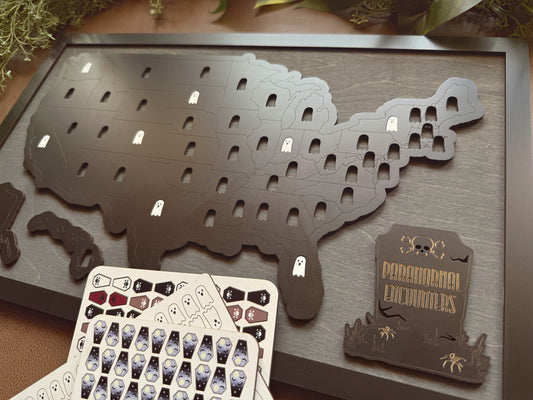 Map of the United States with cut-out states on a wooden surface, accompanied by a card of tokens for tracking