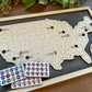 Wooden map of the United States with pins and sticker sheets on a wooden board.